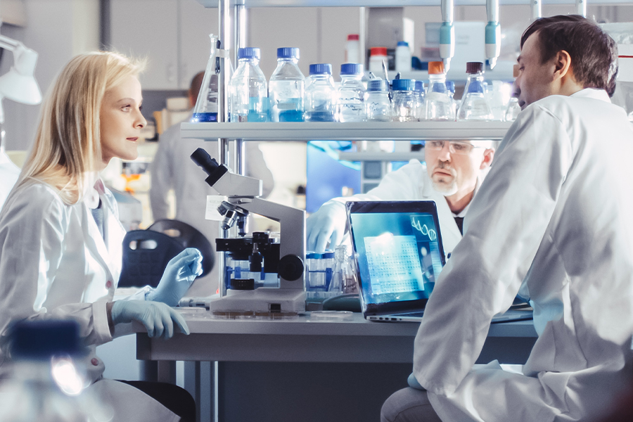 Three scientists sit in lab discussing research
