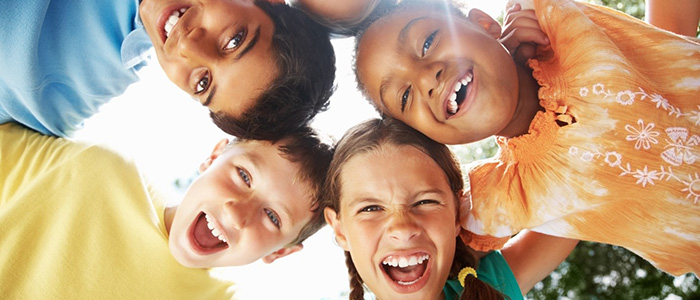 Five young children in a circle, arms around each other's shoulders, looking down at a camera smiling, credit iStock.