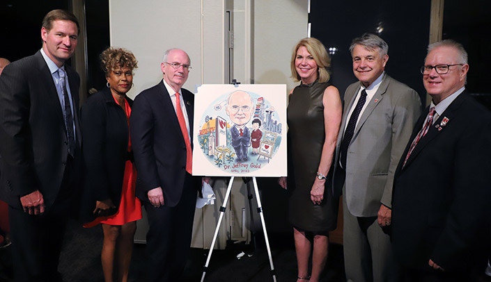 Roasters and roastee, from left: Trev Alberts, athletic director for the University of Nebraska-Lincoln; Aileen Warren, president of ICAN; UNMC Chancellor Jeffrey P. Gold, MD; Omaha Mayor Jean Stothert; James Linder, MD, CEO of Nebraska Medicine; and Rich Watson, UNMC multimedia manager.