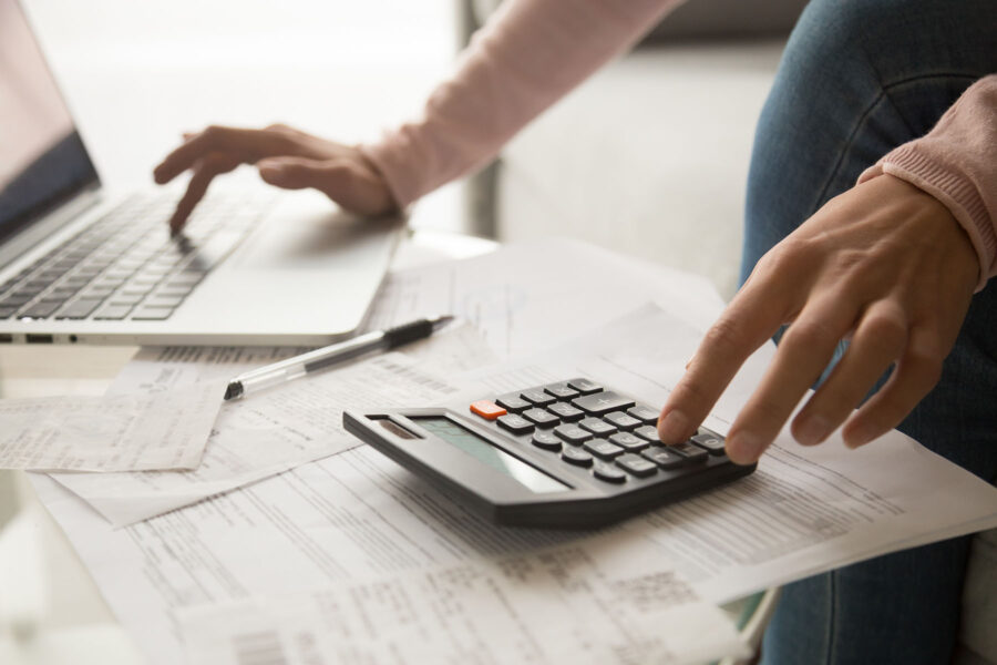 Close up cropped image young woman calculating monthly expenses&comma; managing budget&comma; entering data in computer application&comma; sitting at table full of papers&comma; loan documents&comma; invoices&comma; utility bills&period;