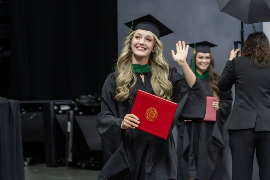 A smiling graduate holding her diploma waves to the crowd&period;