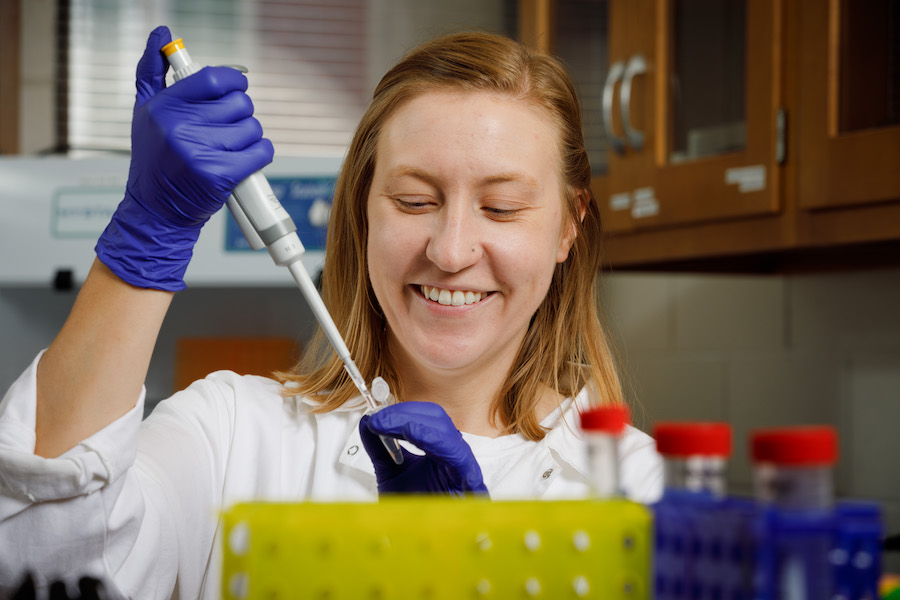 A student smiling while using a pipette in a lab. 