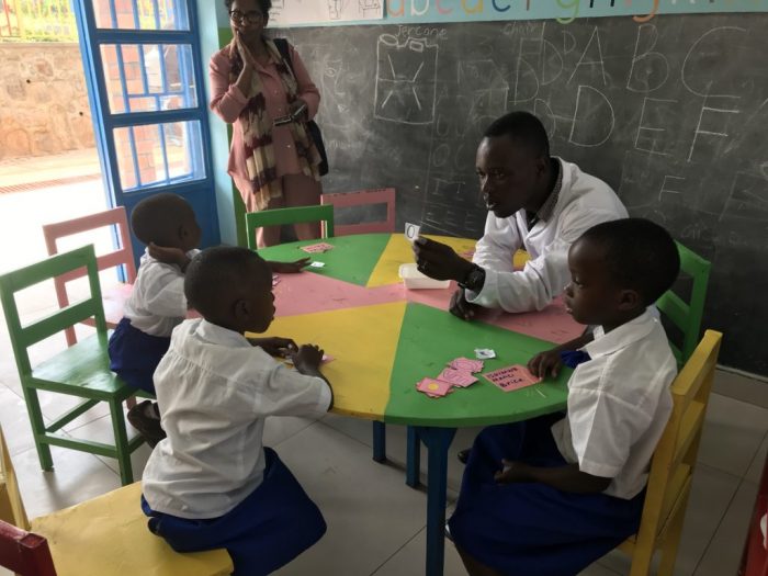A teacher sitting at a school table with 3 young students.