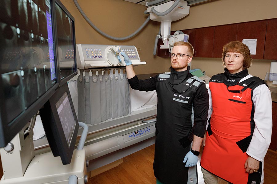 A resident and faculty member perform a scan in an interventional radiology room.