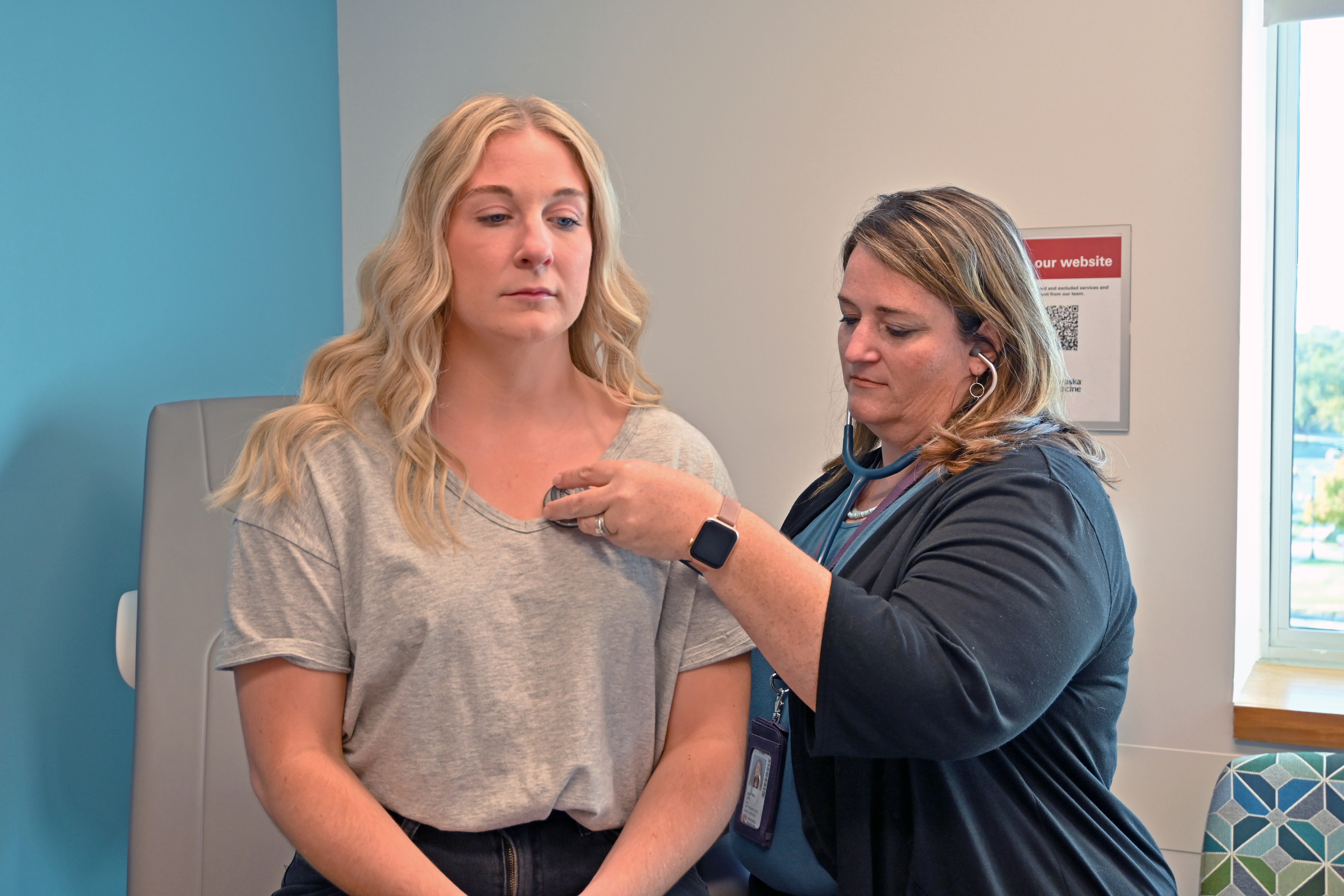 female nurse listening to a female patient's heart with stethoscope