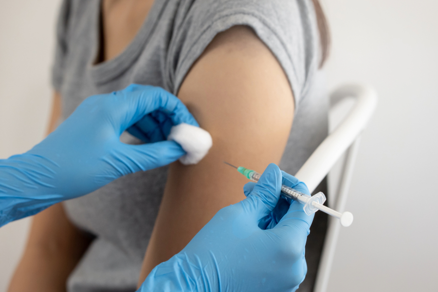 gloved hands providing an immunization shot in a woman's arm