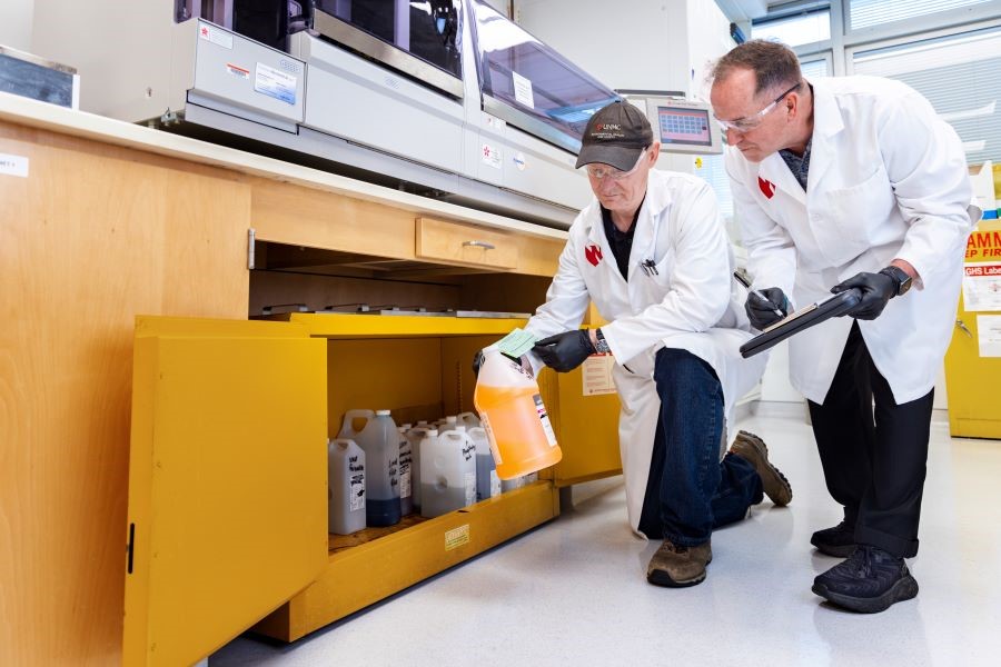 Two institutional biosafety officers conduct routine checks on chemical storage.